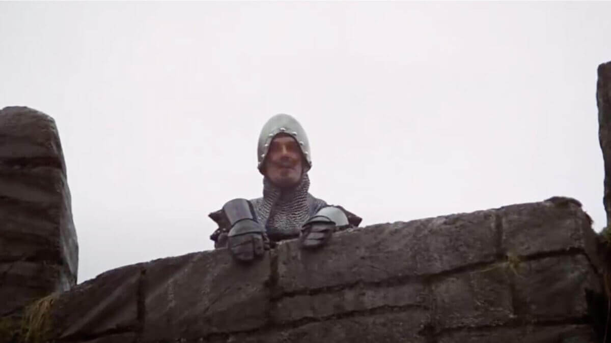 A castle guard peers over a stone wall in Monty Python and the Holy Grail